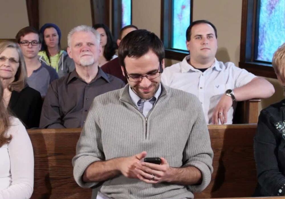 seated man looking at his phone with people seated around him